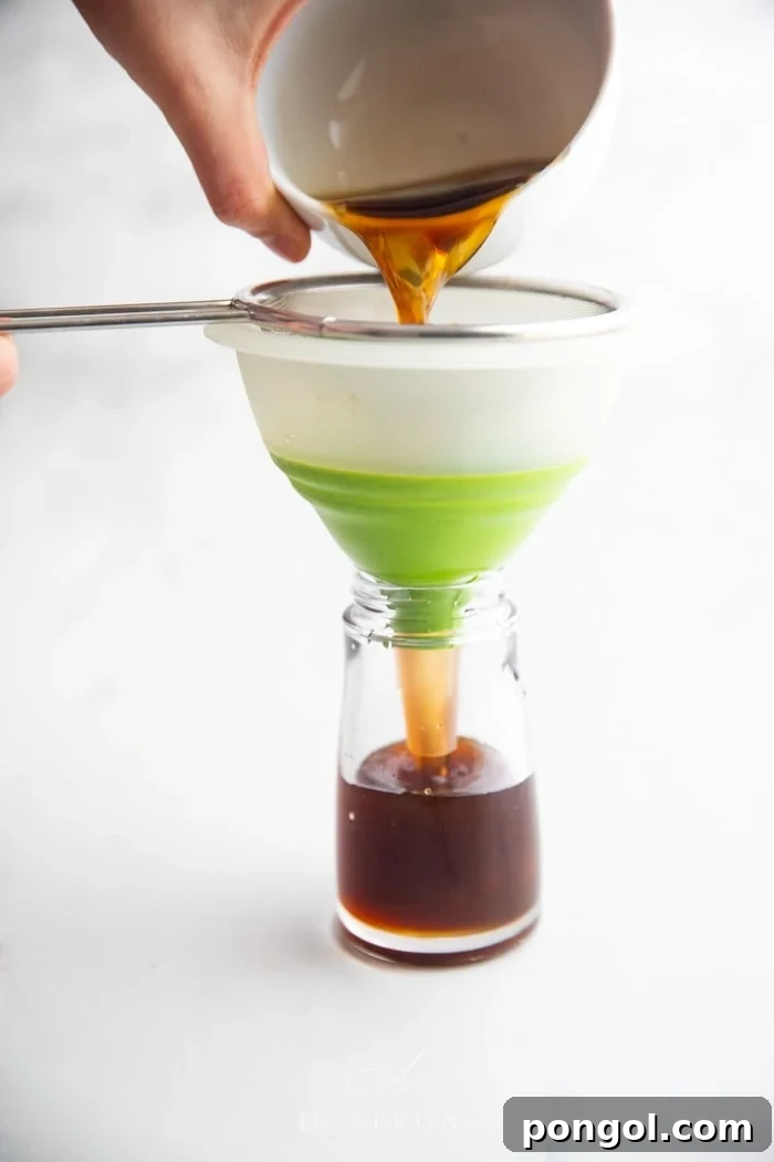 A bowl of soy sauce substitute being strained through a sieve into a bottle, emphasizing the preparation process.
