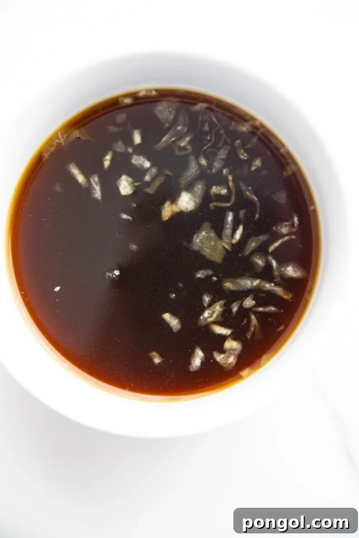 A bowl of soy sauce substitute with small pieces of sauerkraut floating on top before straining, demonstrating a stage of preparation.