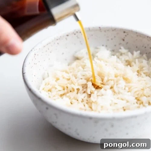 A bottle of soy sauce substitute pouring over a bowl of white rice