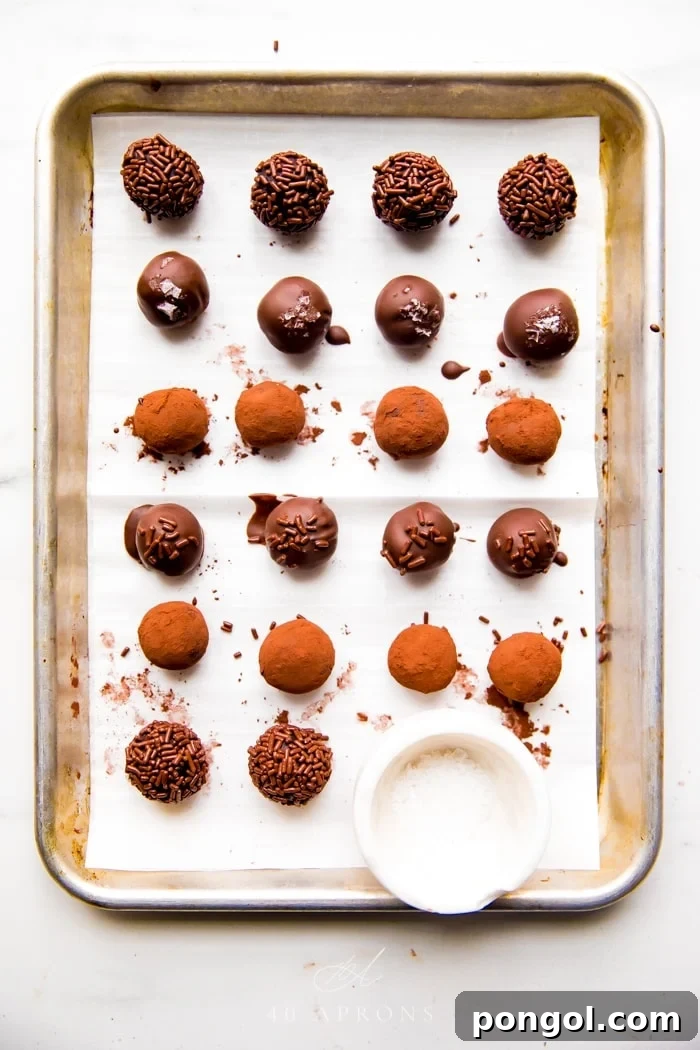 A visually appealing array of healthy vegan truffles with diverse coatings including chocolate dip, cocoa powder, and jimmies, on a baking sheet.