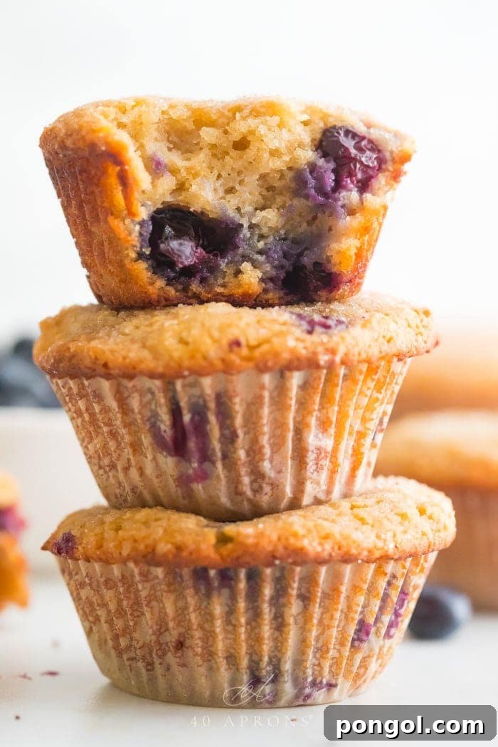 A stack of three paleo blueberry muffins with a bite taken out of one, showcasing juicy blueberries inside.