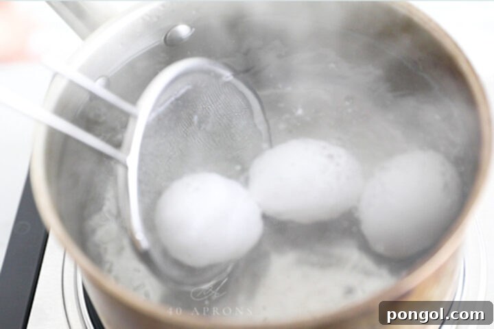 A handheld strainer lowering eggs into hot water.