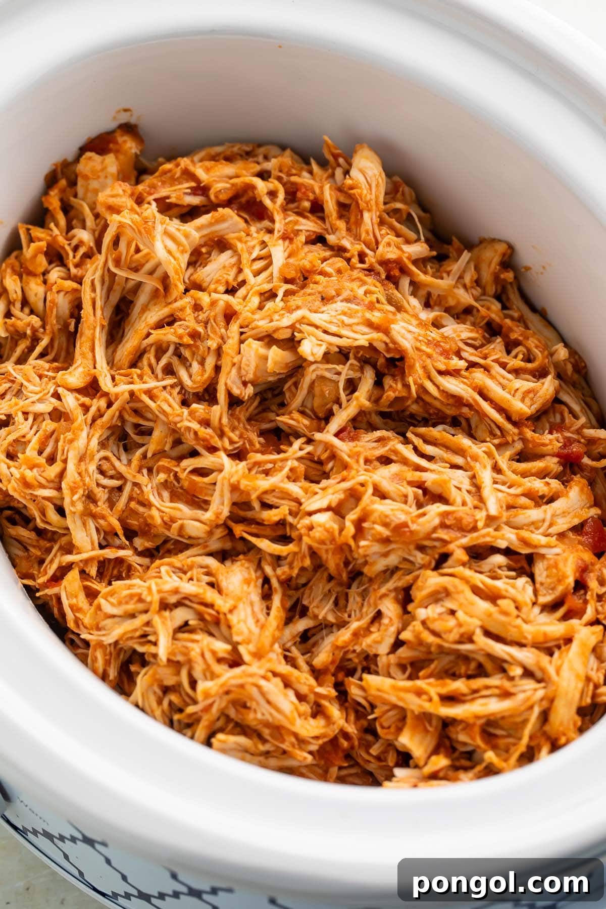 Shredded Mexican chicken in a white slow cooker on a kitchen counter.