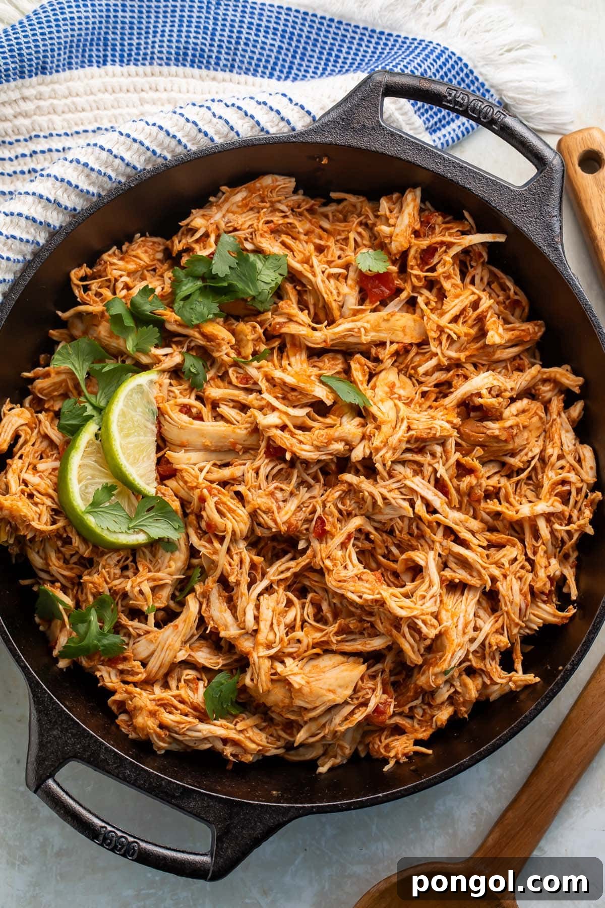 Slow cooker shredded Mexican chicken in a large cast-iron skillet, garnished with lime wedges and cilantro.