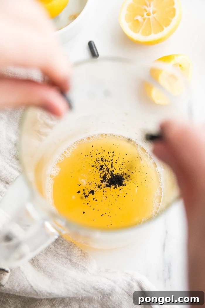 A capsule of activated charcoal being opened and poured into a pitcher, showing the fine black powder