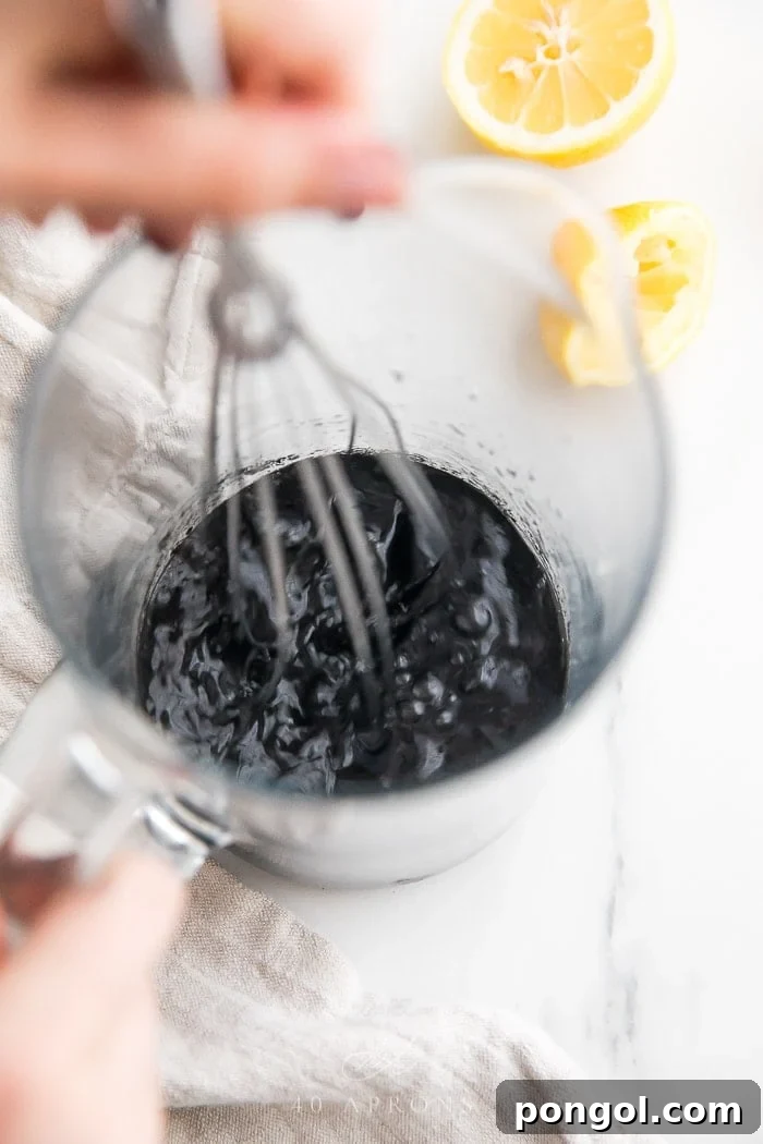 A whisk stirring charcoal lemonade ingredients in a pitcher, demonstrating the mixing process