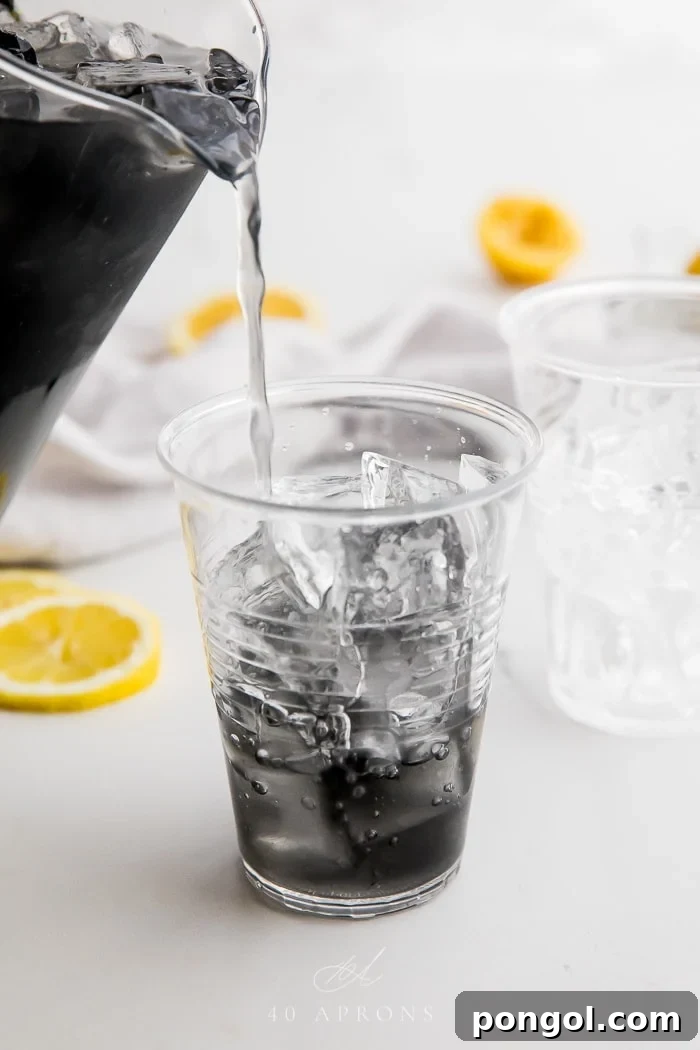 Pitcher pouring charcoal lemonade over ice into a glass, showcasing the final refreshing drink