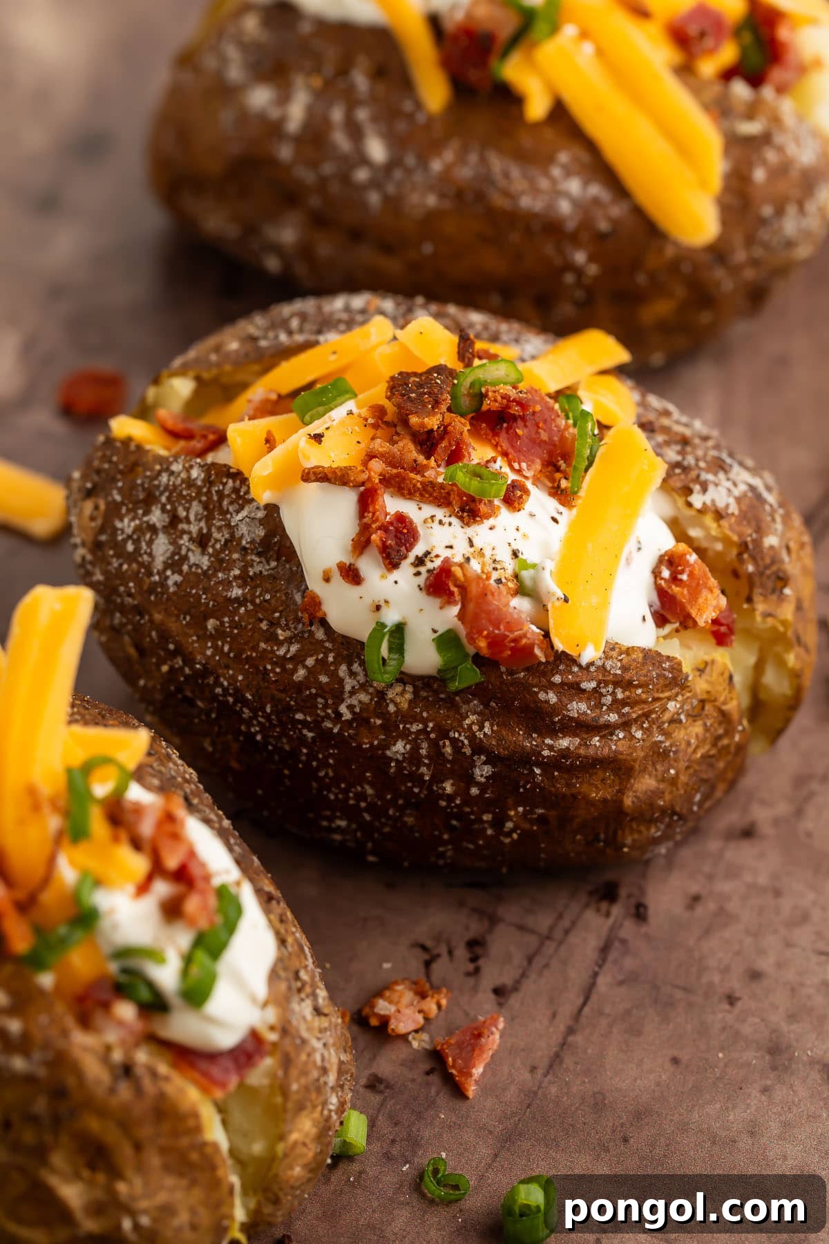Grilled baked potato split open, piled high with sour cream, shredded cheddar cheese, green onions, and crumbled bacon, ready to be enjoyed.