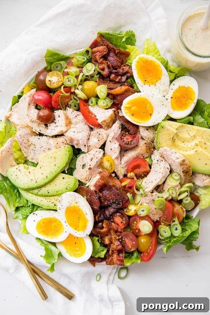 A beautifully arranged classic healthy chicken cobb salad on a pristine white plate, showcasing its vibrant ingredients like chicken, bacon, avocado, and jammy eggs, drizzled with ranch dressing.