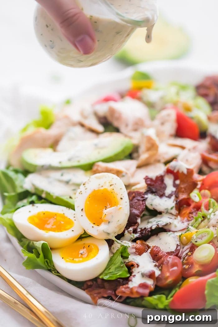 Creamy ranch dressing being drizzled generously over a vibrant and classic chicken healthy cobb salad, highlighting its rich textures and colors.