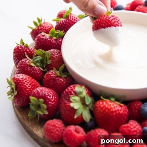 A bowl of creamy vanilla yogurt fruit dip with a fresh strawberry being dipped into it, ready to be enjoyed.