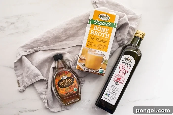 Sprouts organic maple syrup, bone broth, and olive oil bottles arranged on a gray towel.