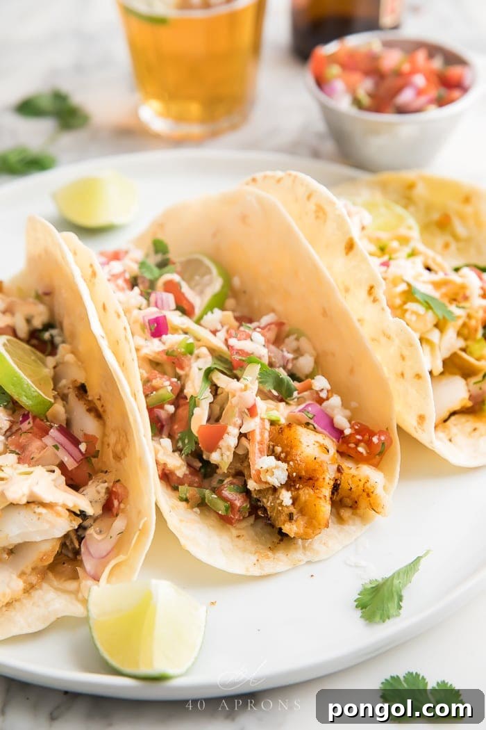 Three beautifully arranged easy fish tacos on a pristine white plate, accompanied by vibrant lime wedges, ready to be enjoyed as a refreshing and flavorful meal.