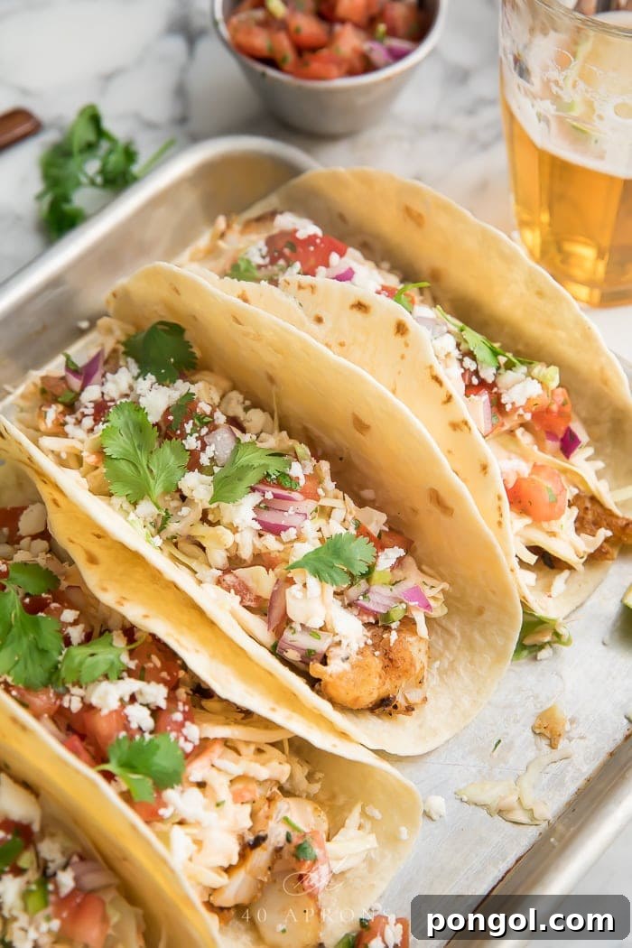 Three perfectly crafted easy fish tacos presented on a sleek metal tray, elegantly garnished with fresh herbs and a slice of lime, embodying a fresh and appetizing meal.