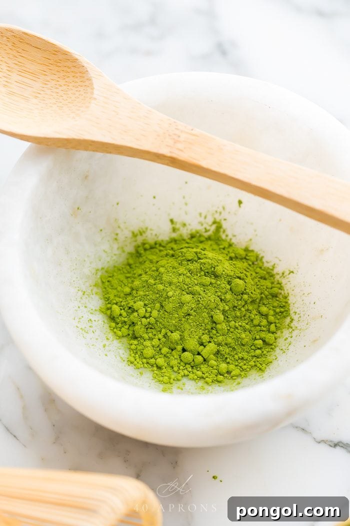 A white ceramic bowl filled with bright green matcha, accompanied by a traditional bamboo spoon and whisk, ready for preparation.