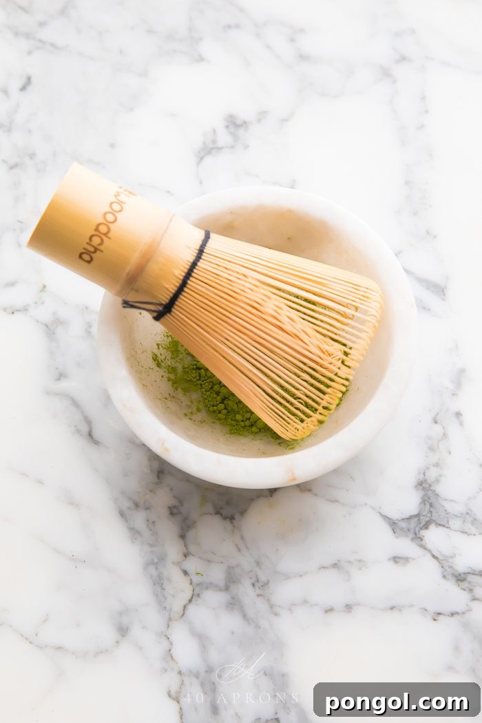 A traditional bamboo whisk (chasen) placed gently in a bowl of vibrant green matcha, ready for the tea ceremony.