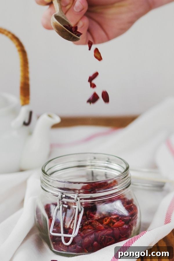 Dried cranberries being carefully spooned into a clear glass mason jar, showcasing their vibrant red color.