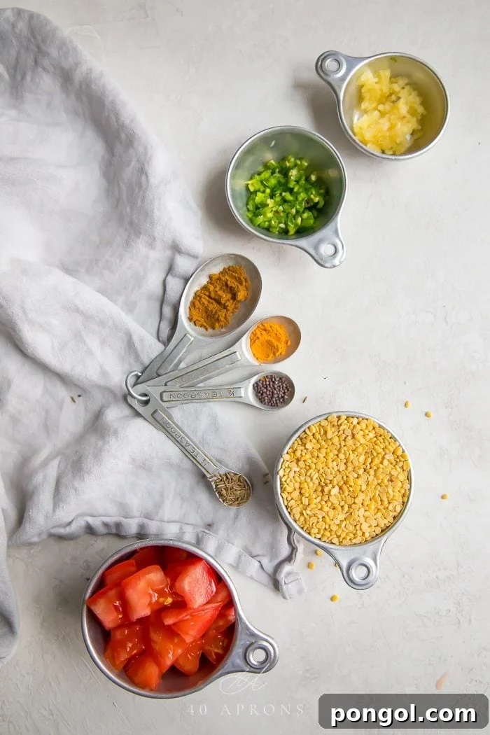 Ingredients to make the dish laid out on a white work surface: yellow lentils, spices, tomato, garlic, green chili, and oil