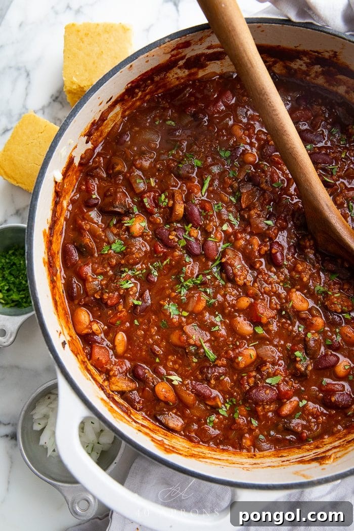 A large pot of vibrant vegan chili simmering on the stove, stirred by a wooden spoon, showcasing its rich texture and color.