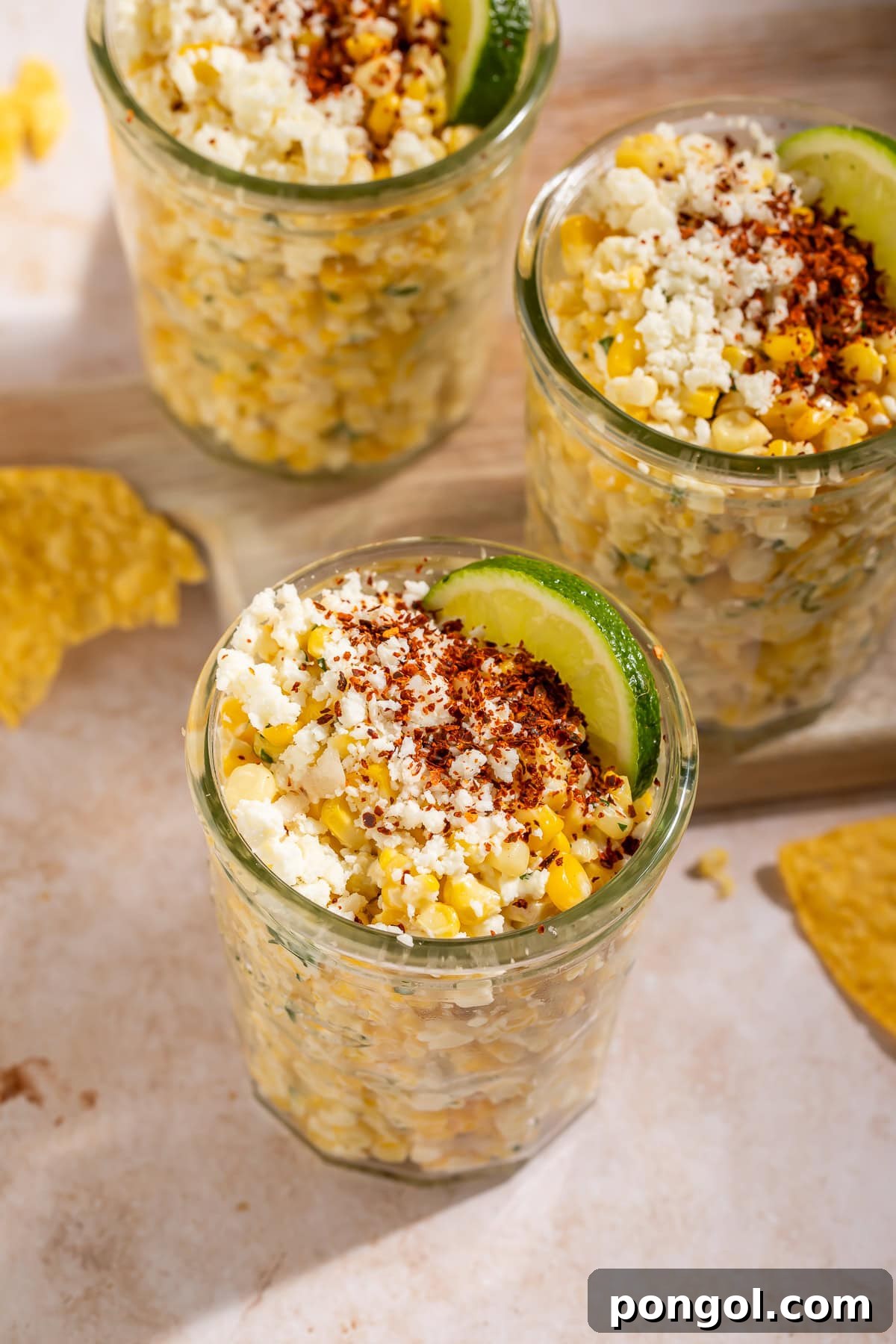 Close-up view of Mexican Street Corn (Esquites) served in a mason jar, garnished with crumbled cotija cheese and a dusting of chili powder.