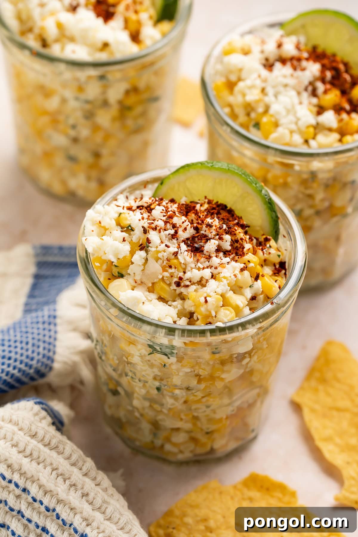 Close-up of a single mason jar filled with Esquites (Mexican Street Corn Salad), topped with crumbled Cotija cheese, chili powder, and a fresh lime wedge, ready to be enjoyed.