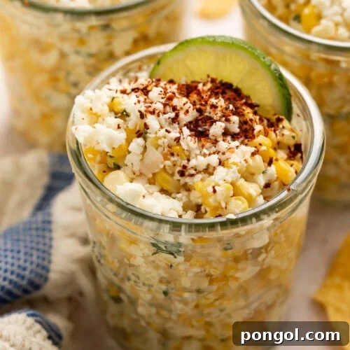 Three glass jars filled with Mexican street corn topped with crumbled cheese, chili powder, and lime wedges