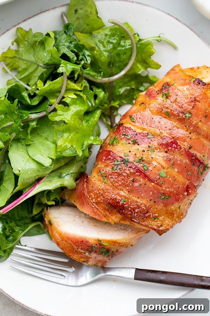 Close-up of bacon wrapped chicken served with a side salad on a white plate, ready to eat.