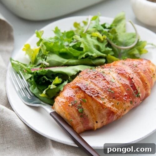 Bacon wrapped chicken served on a plate with a salad and a fork