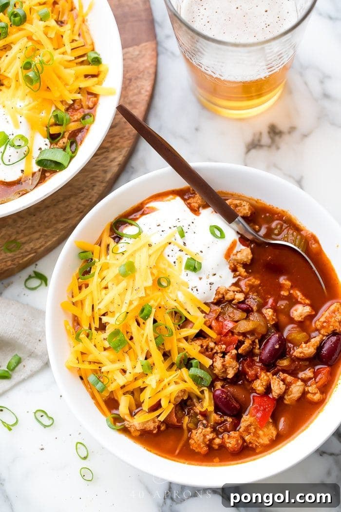 Turkey chili served in a white bowl with fresh toppings like cilantro and cheese, ready to eat.
