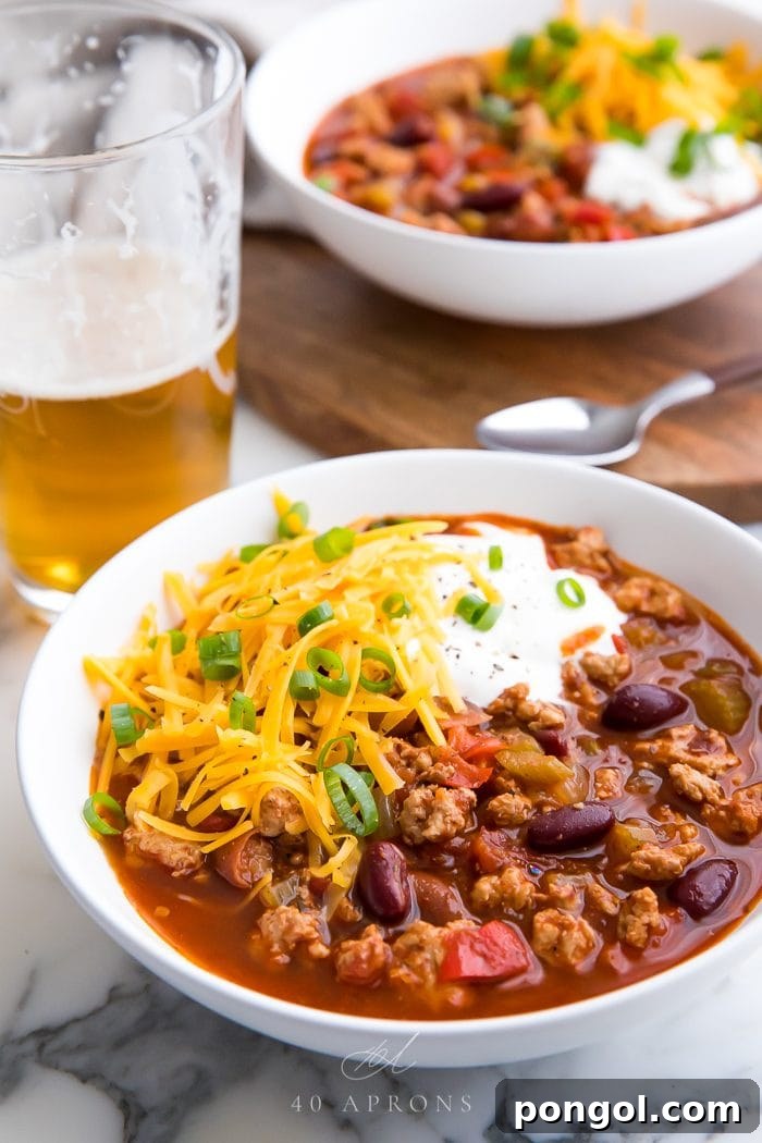 Two white bowls filled with hearty slow cooker turkey chili, topped generously with cheese, green onions, and sour cream.