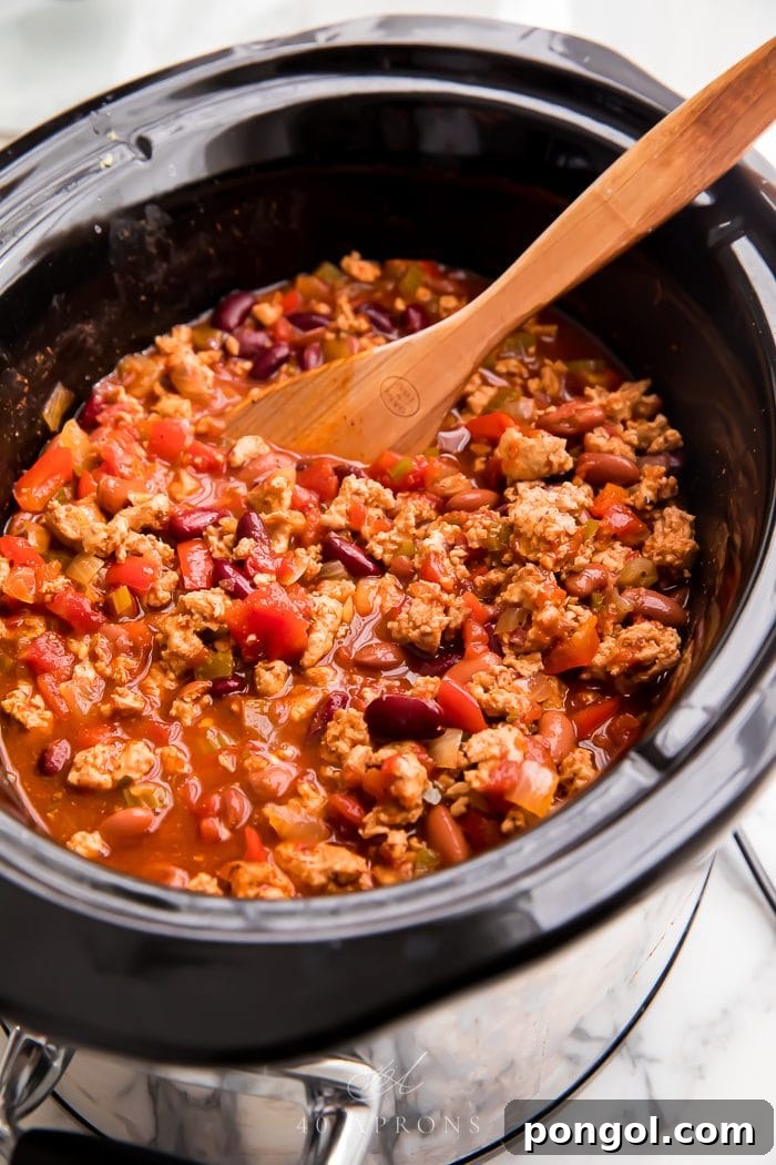Rich turkey chili simmering gently in a vibrant red slow cooker, creating a warm and inviting scene.