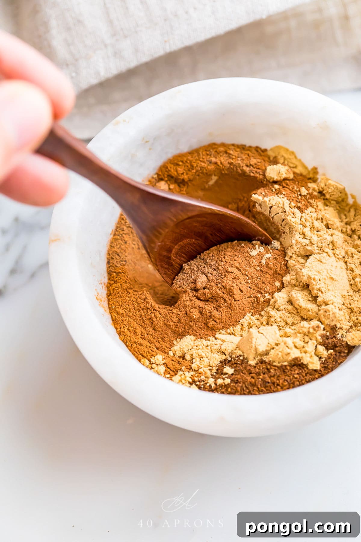 Spices being stirred together with a wooden spoon in a small marble bowl to make a homemade pumpkin pie spice blend.