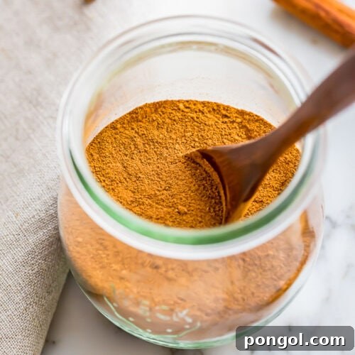 Homemade pumpkin pie spice blend in a glass jar with a wooden spoon.
