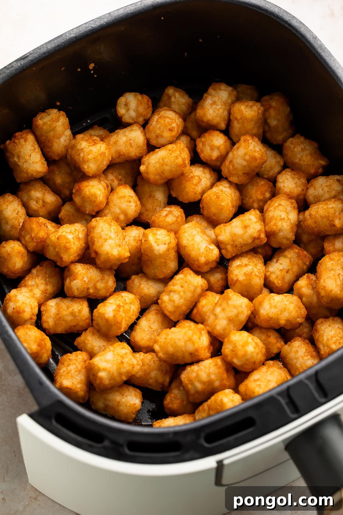 Golden, crispy tater tots overflowing in a black air fryer basket, steam gently rising.