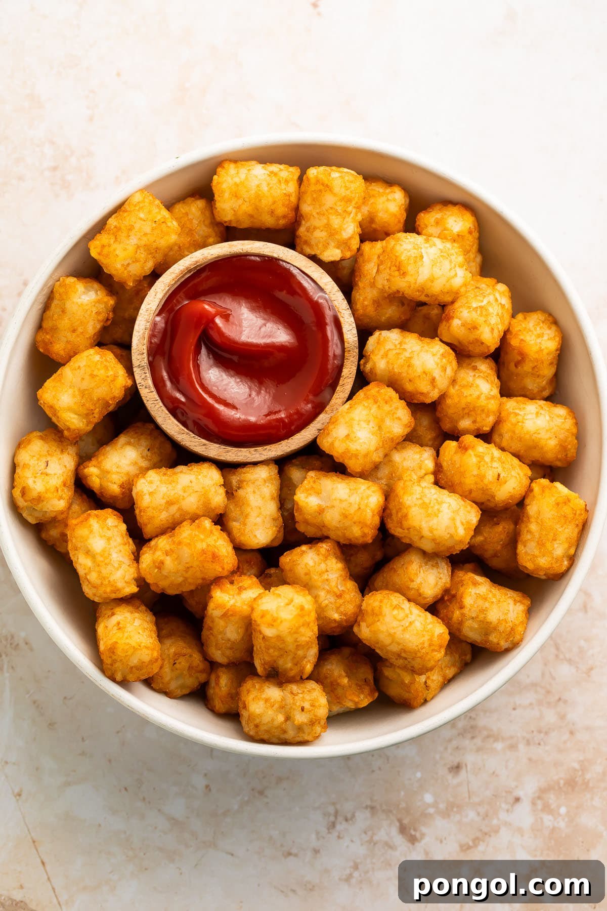 Overhead shot of a large, inviting bowl filled with crispy air-fried tater tots, beautifully arranged with a small ramekin of vibrant red ketchup for dipping.