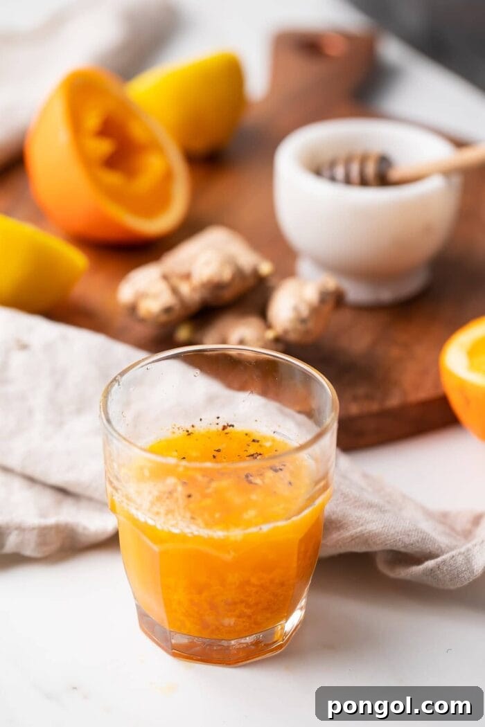 A vibrant immunity booster shot in a glass, with all the natural ingredients laid out in the background, including fresh ginger, garlic cloves, lemons, oranges, and spices.