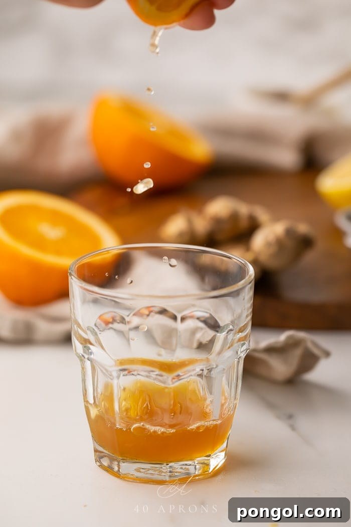 A hand squeezing fresh orange juice directly into a glass, highlighting the use of fresh ingredients for the immune booster shot recipe.