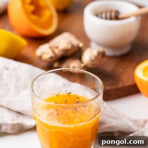 An immunity booster shot in front of the ingredients, a close-up shot of the vibrant yellow drink.