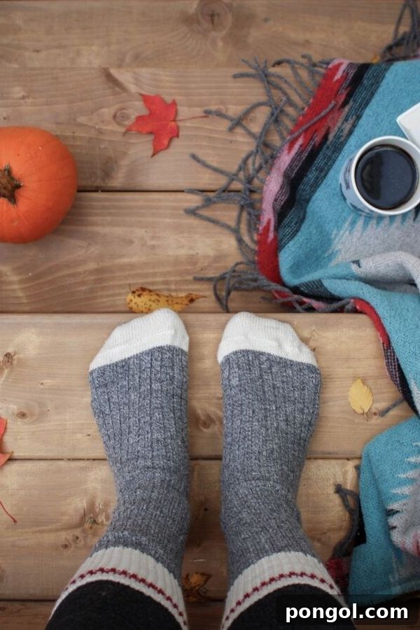 A woman's feet in thick, cozy socks resting on a rustic wooden floor, surrounded by a pumpkin, a scarf, and a coffee mug, embodying autumn comfort.
