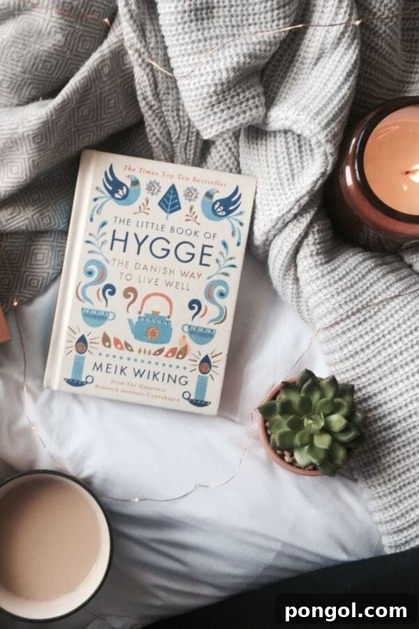 Overhead shot of 'The Little Book of Hygge' by Meik Wiking lying on a bed, next to a lit scented candle and a mug of coffee.