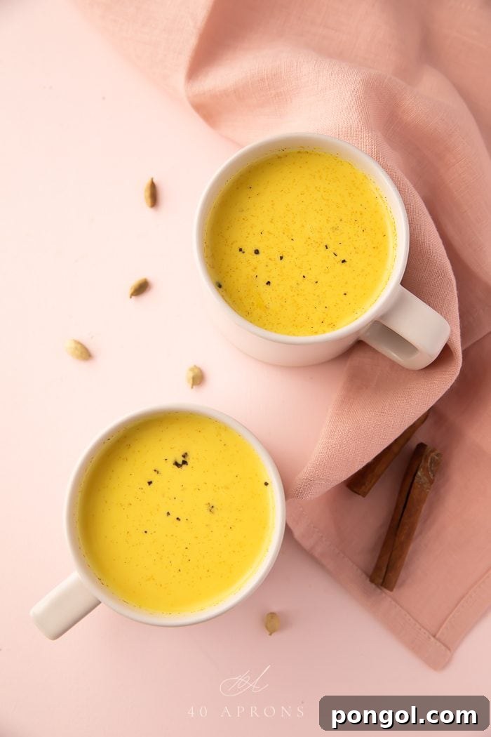 Two white mugs filled with golden milk, garnished with a sprinkle of cinnamon and a cinnamon stick, on a rustic wooden surface. The warm, inviting glow of the drink is prominently featured.