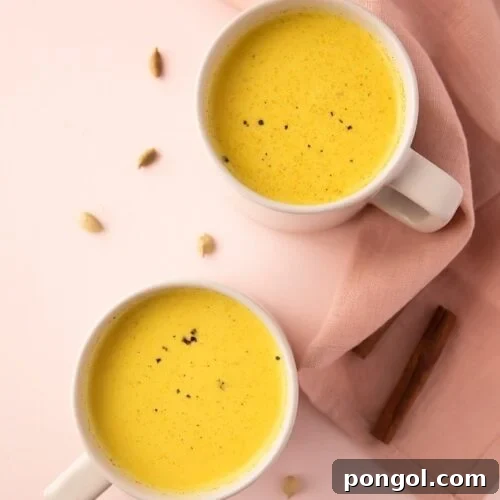 Two mugs of golden milk, one in the foreground slightly out of focus, emphasizing the rich color and inviting nature of the drink.