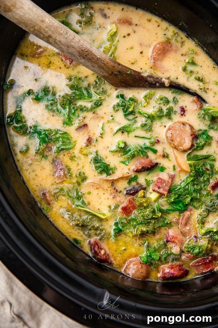 Hearty Whole30 Crockpot Zuppa Toscana 3 A spoon gently stirring the creamy Zuppa Toscana in a slow cooker, showcasing the rich texture and colorful ingredients.