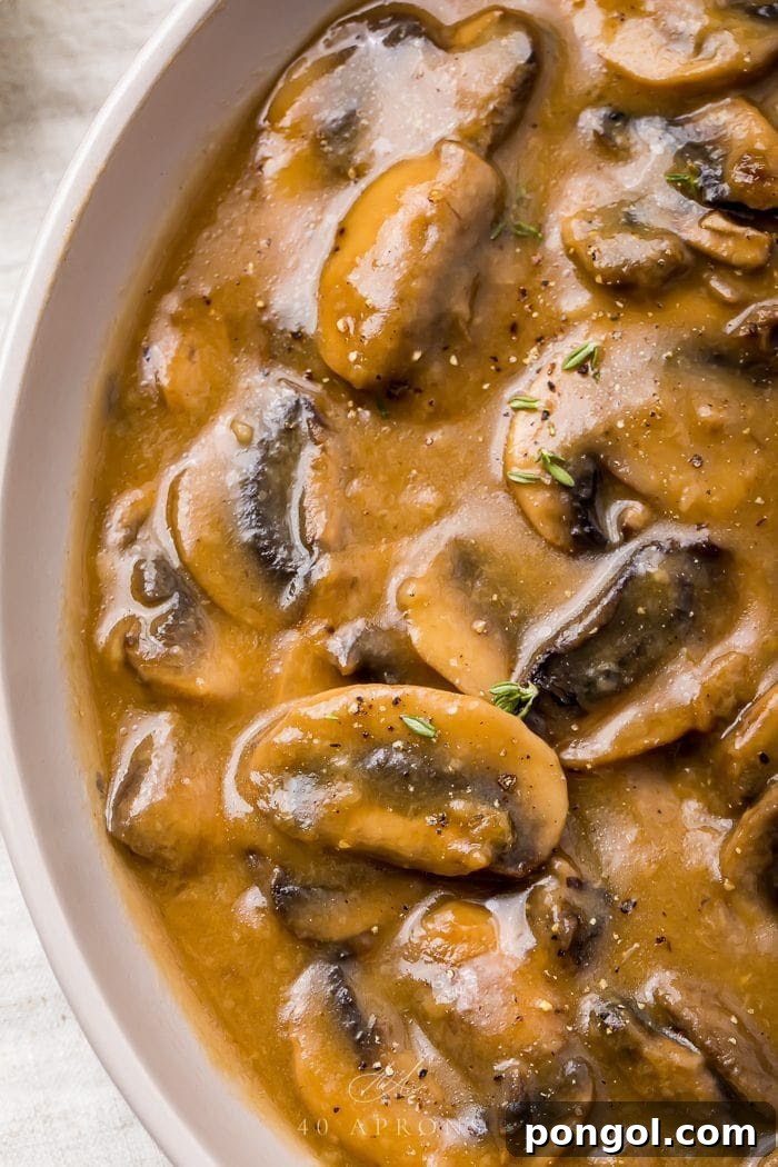 A close-up of rich, brown mushroom gravy in a white ceramic bowl, garnished with fresh herbs, showcasing its thick and smooth texture.