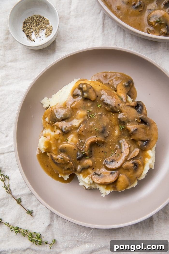 A plate featuring a generous serving of mashed potatoes topped with rich mushroom gravy and a sprinkle of fresh green herbs.