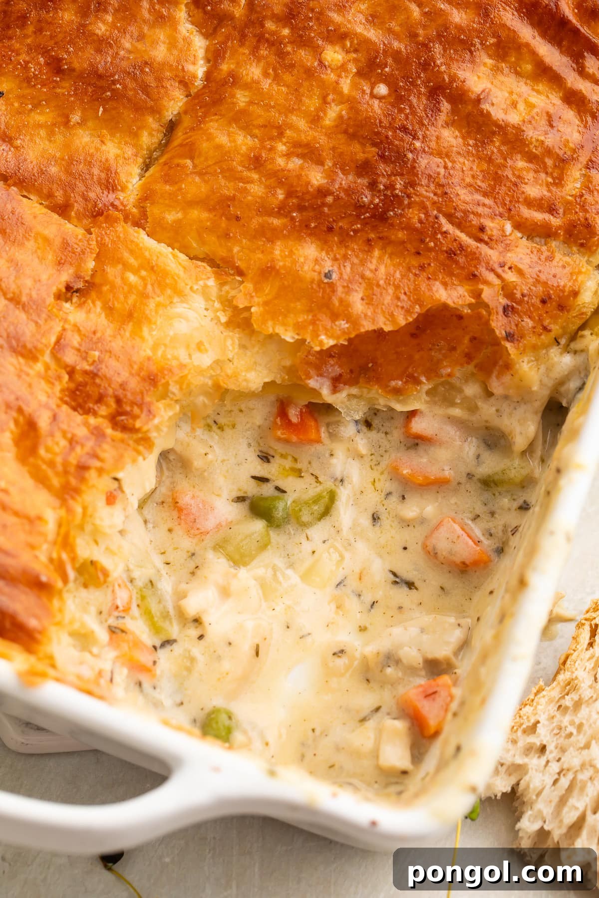 A square baking dish filled with a golden-brown chicken pot pie casserole, with a section scooped out to reveal the rich, creamy filling of chicken and vegetables beneath the flaky crust.