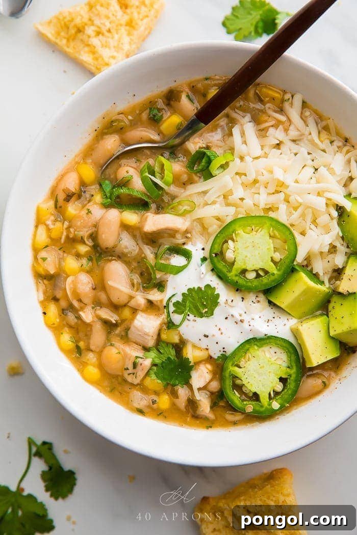 A inviting white bowl of creamy white bean chili, generously topped with fresh cilantro, avocado slices, and a dollop of sour cream, emphasizing its rich texture and vibrant garnishes.