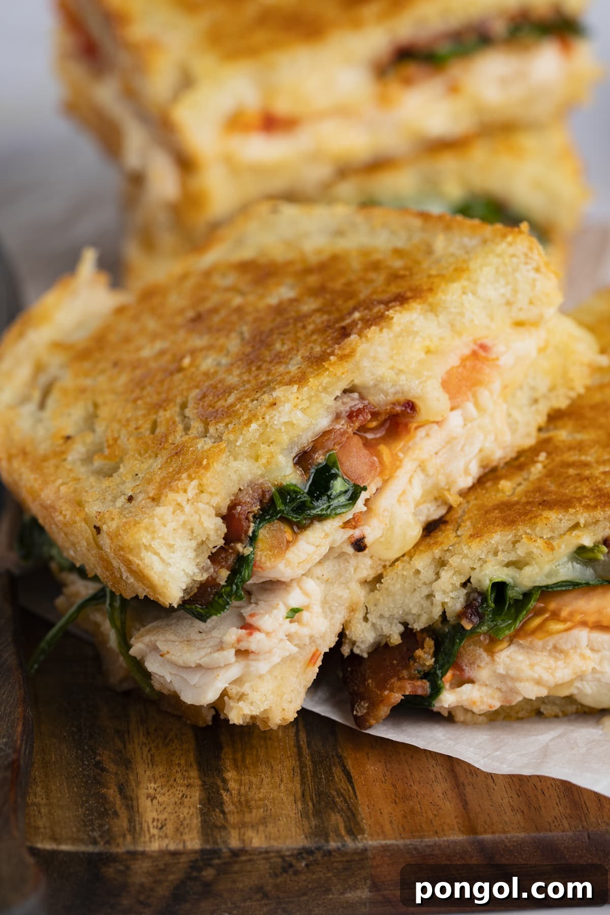 A golden-brown turkey melt sandwich, generously filled with spinach, crispy bacon, and gooey melted cheddar cheese, perfectly grilled and presented on a rustic wooden cutting board.
