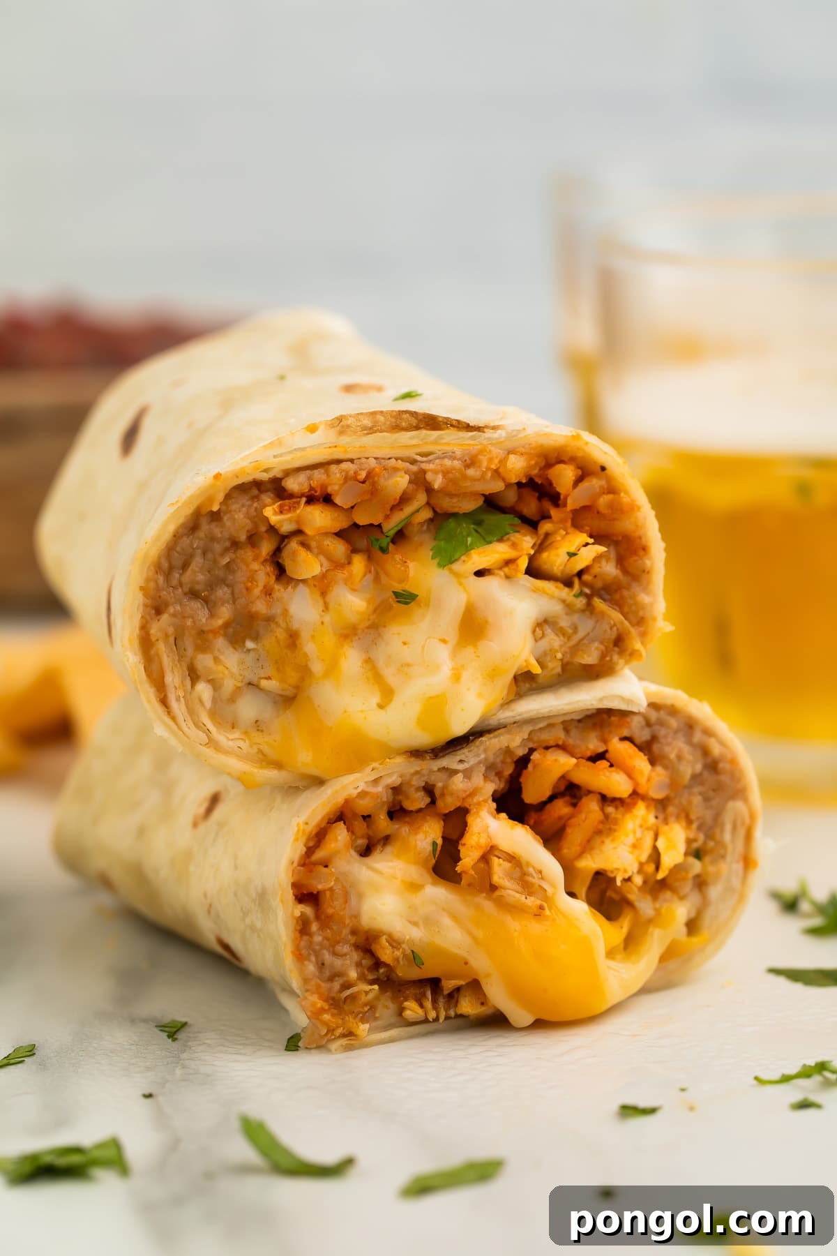 Two halves of a perfectly stacked chicken burrito, expertly cut to reveal a mouth-watering filling of seasoned chicken, fluffy rice, savory beans, and oozing melted cheese.