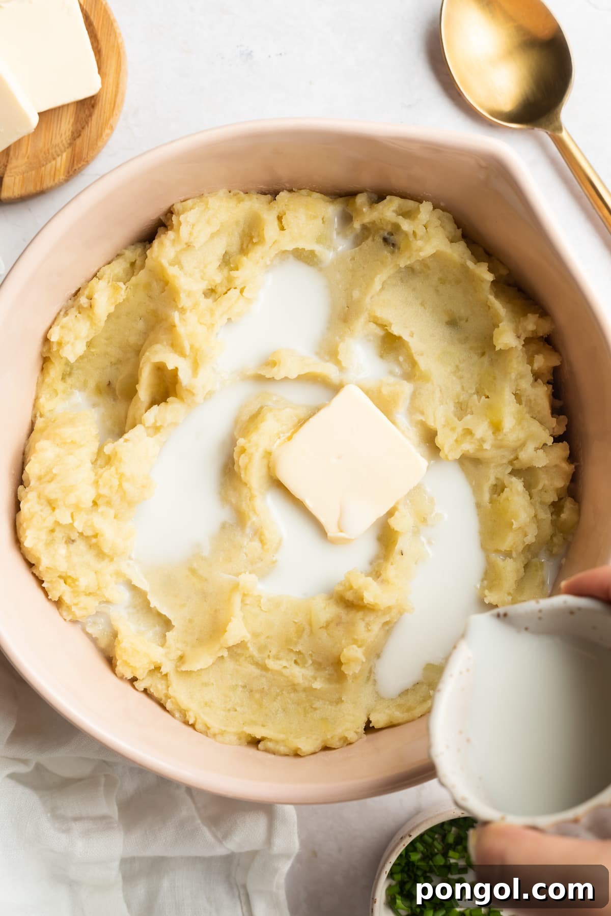 A large bowl of fluffy mashed potatoes, generously topped with melting butter and a drizzle of milk, ready for reheating or repurposing, highlighting their creamy texture.